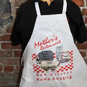 black polo tshirt wearing a white apron with Mothers restaurant" and "New Orleans Home cooking" red print and an image of foods printed on the apron